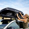 Hapro dakkoffertassen laden op auto – ideaal voor vakantie en roadtrip Vrouw plaatst bagage in Hapro dakkoffer op auto bij strand – extra bagageruimte voor vakantie