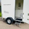 Mobiele badkamer met toilet op aanhanger Mobiele badkamer aanhanger met toilet en wastafel zichtbaar via open deur