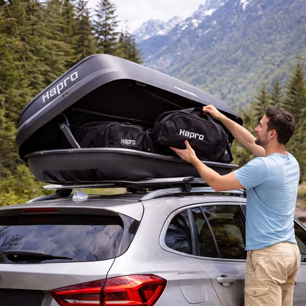 Hapro dakkoffer in gebruik tijdens vakantie in de bergen Man plaatst bagage in Hapro dakkoffer op auto in bergachtig landschap tijdens vakantie